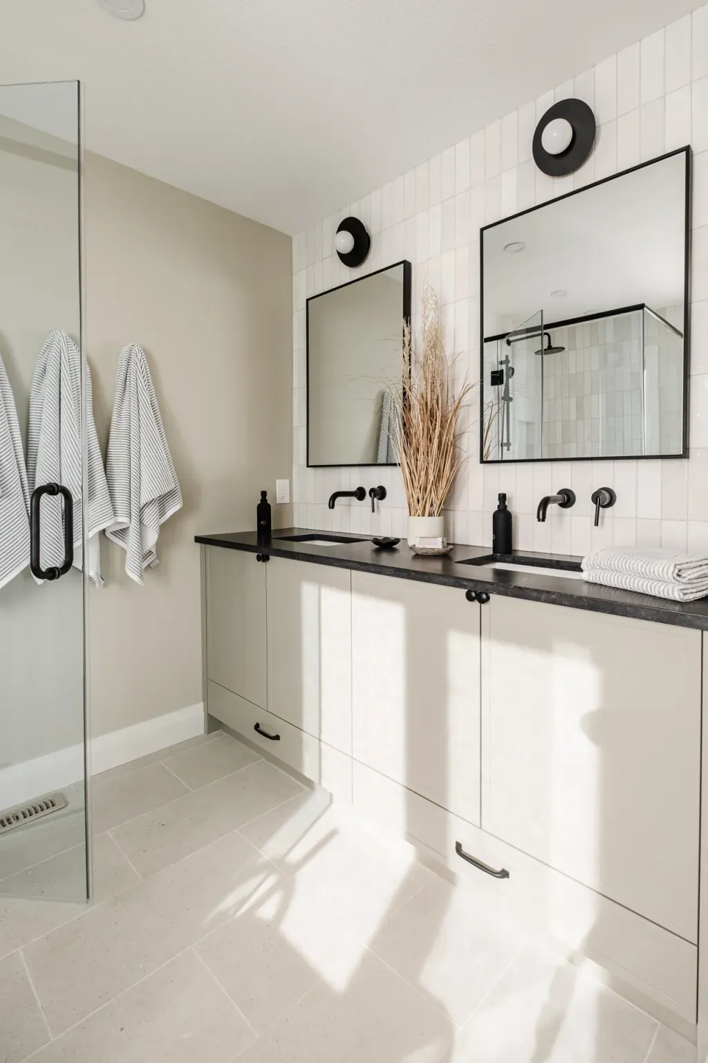 a bathroom vanity with double sinks, black countertop, and off-white cabinets, walls, and floor tile