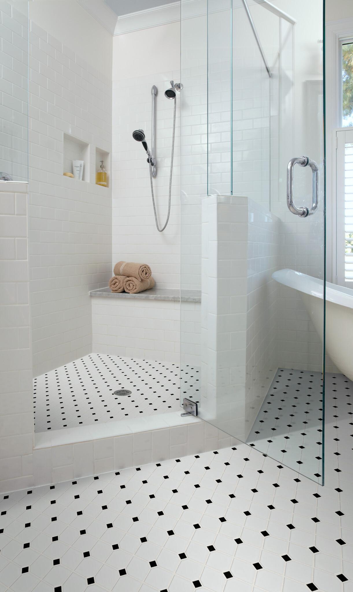 a shower with a glass door and white tile floor and windows, with black dots on the floor