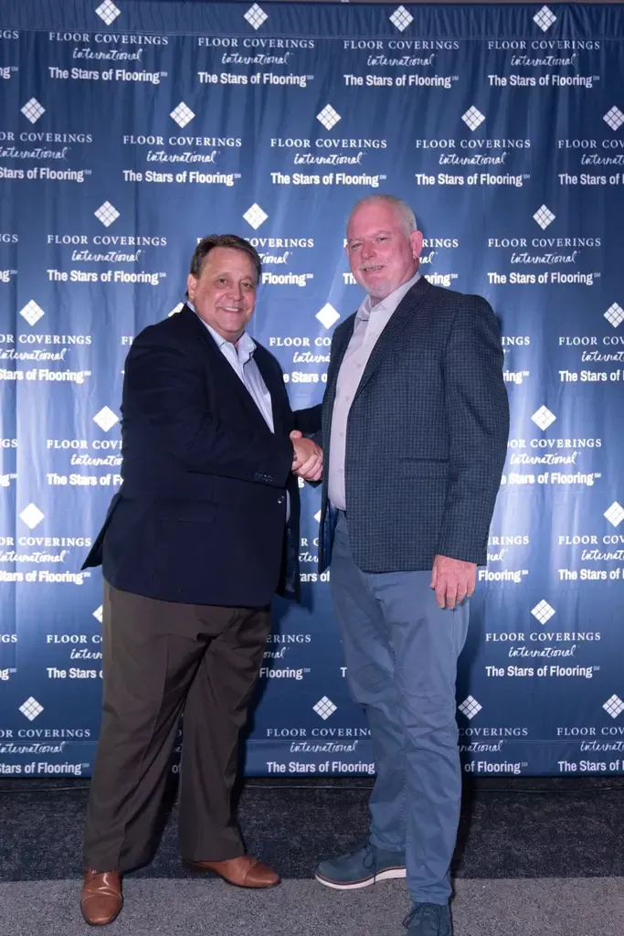 Two men shaking hands in front of a blue wall, symbolizing partnership in engineered flooring solutions for Florida.