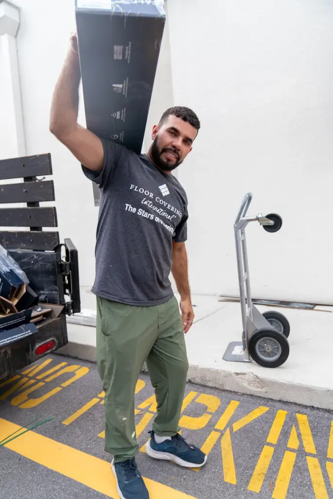 A man lifts a large piece of furniture into a truck, with a backdrop of laminate flooring in Wellington, FL.