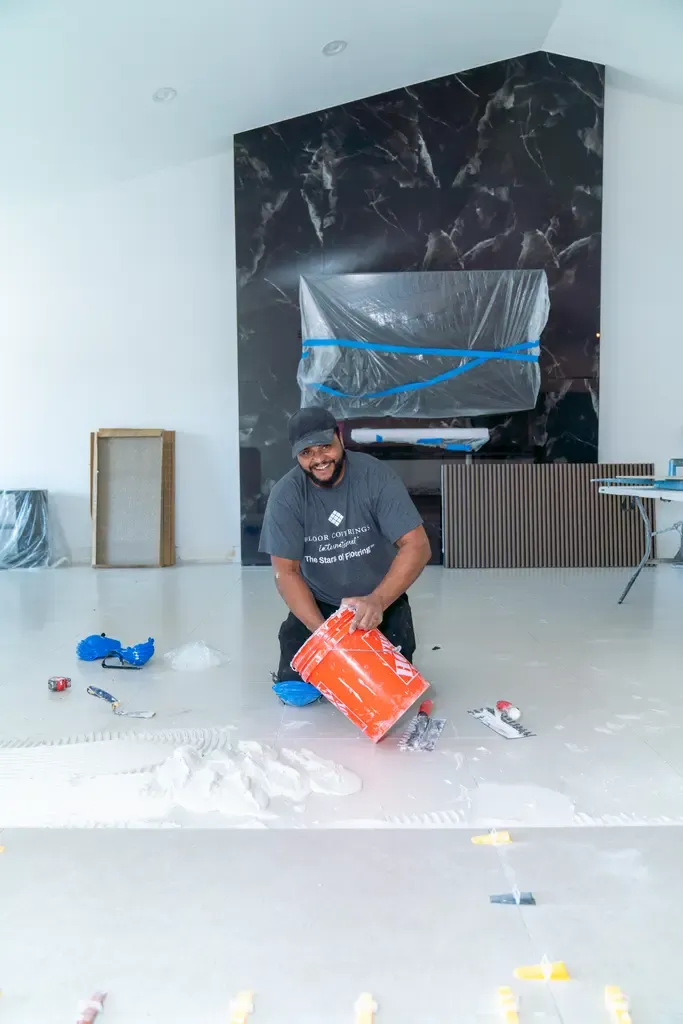 A man is laying a large white tile on the floor, demonstrating tile flooring work in Wellington, FL.