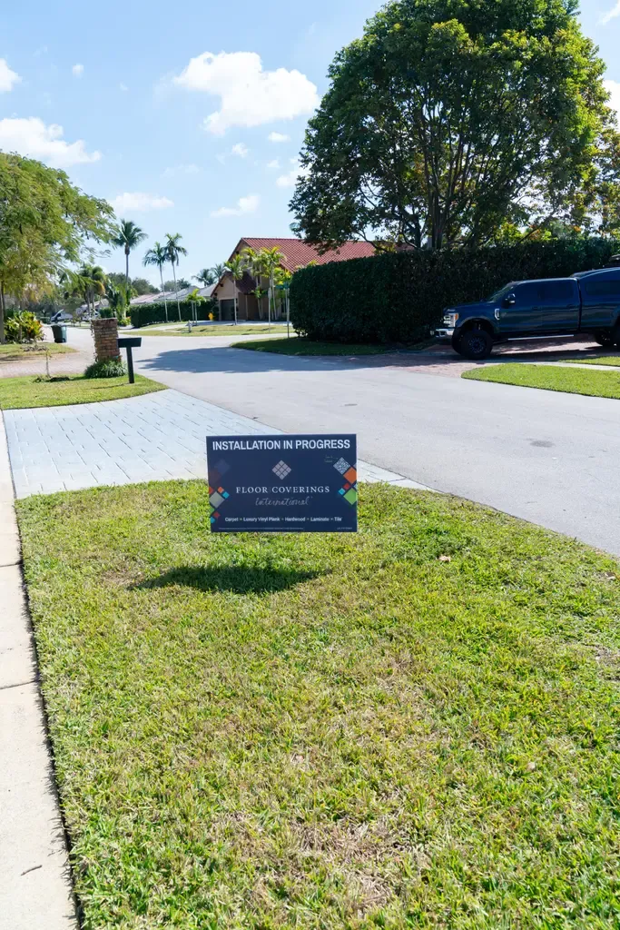 Home for sale sign in a Wellington, FL neighborhood, highlighting vinyl flooring features.