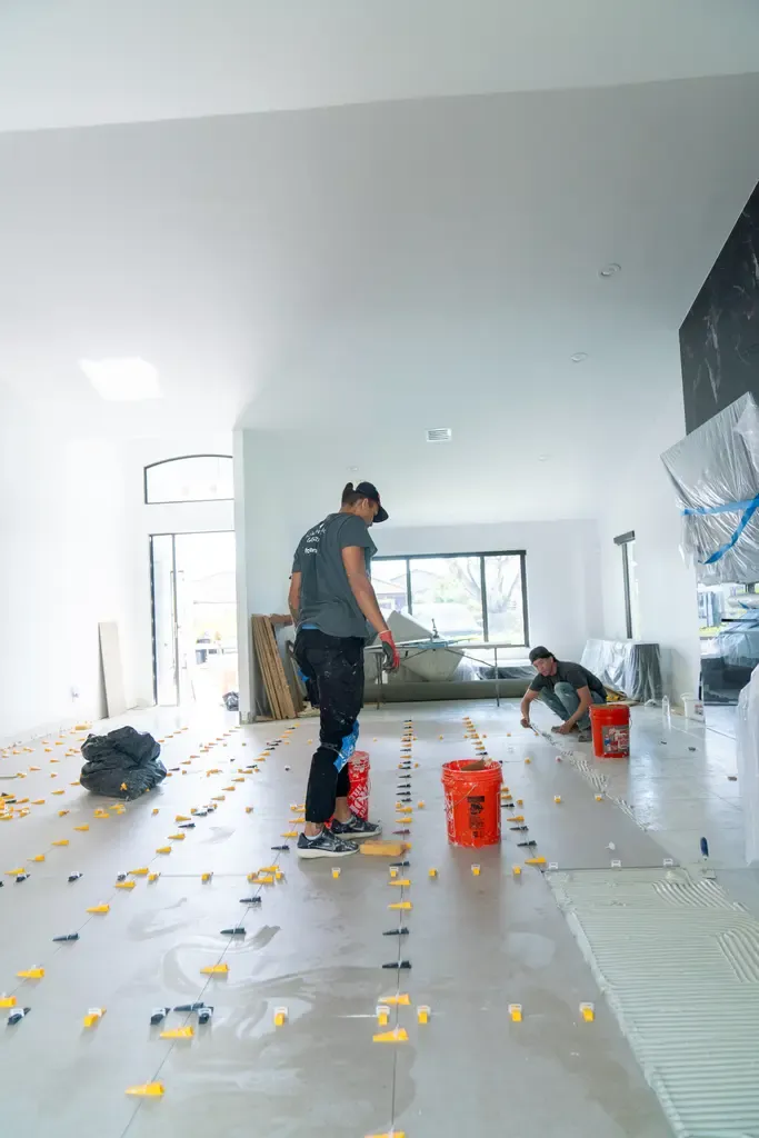 Two workers laying tile on the floor of a large room in Wellington, FL.