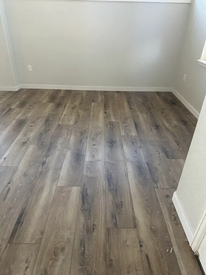 Interior view of a room with wood flooring and white walls, highlighting 3.25 inch baseboards, floor vents, and trim.