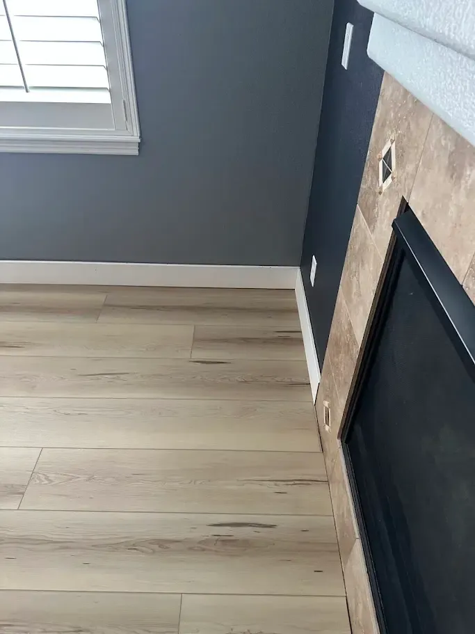 A warm living space with a fireplace, wooden floors, and a window, displaying 5 inch baseboards and floor vents.