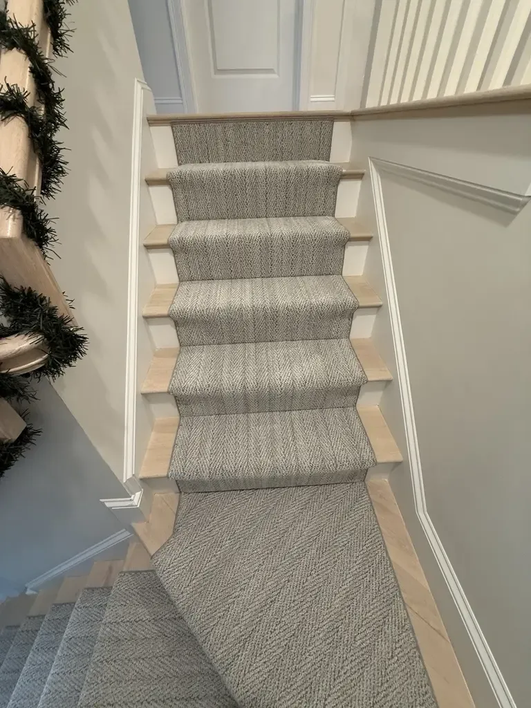 A carpeted stairway leading to a wood-floored area in Foxboro, MA, showcasing a blend of textures and materials.