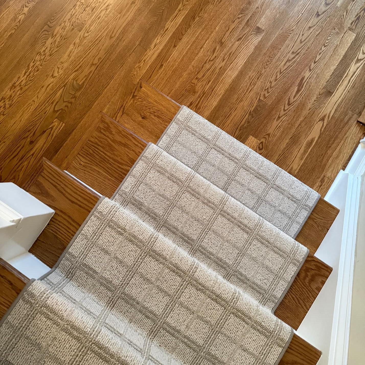  A top view of a hardwood staircase with a beige carpet runner.