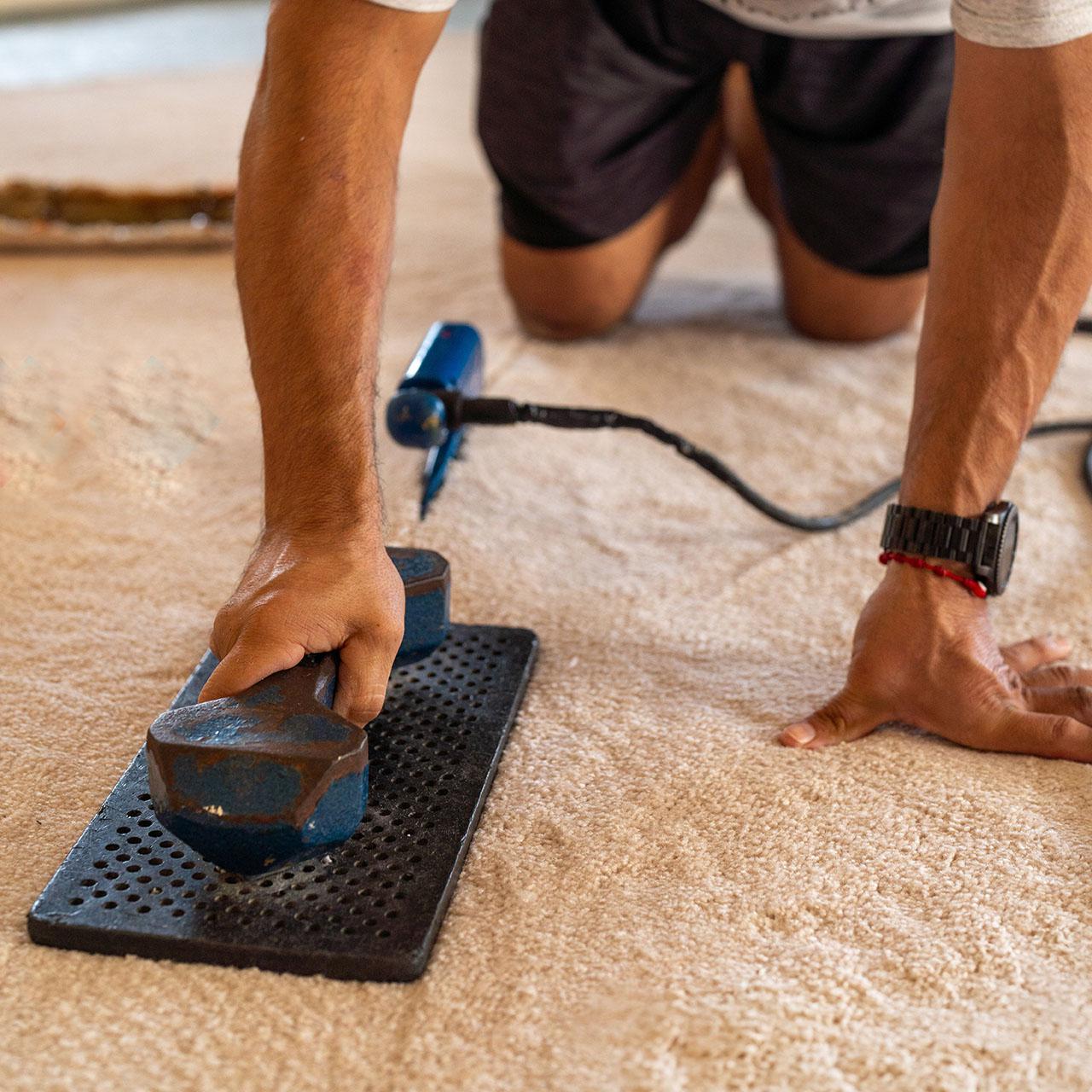 A man is sanding a carpet with a power tool, aiming to achieve a smooth finish on the carpeted floor.