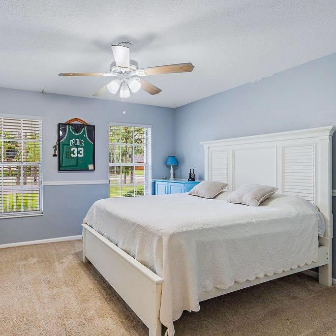 A stylish bedroom showcasing a white bed, a ceiling fan, and warm carpet flooring.