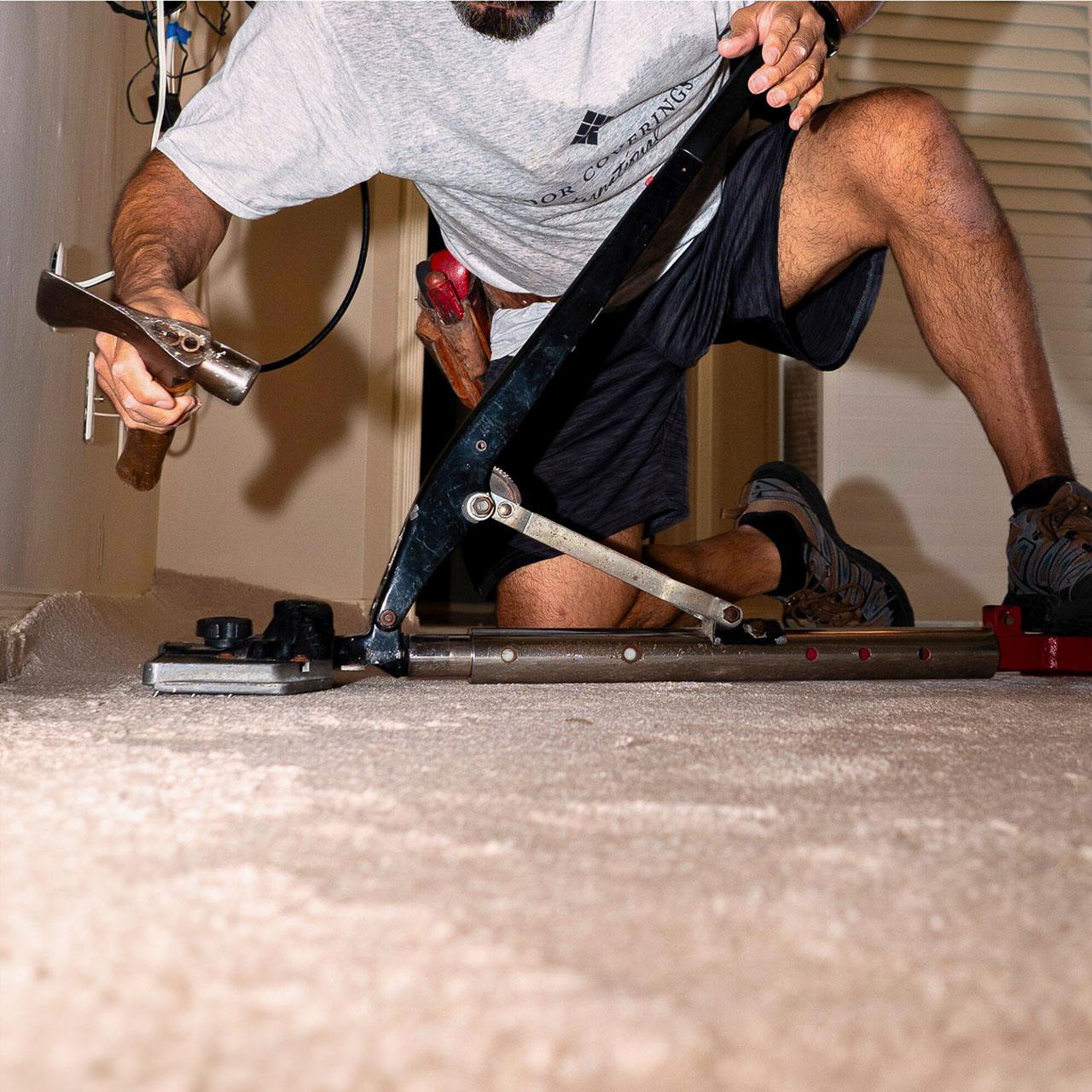 A man is engaged in installing carpet flooring, demonstrating craftsmanship in a bright environment.