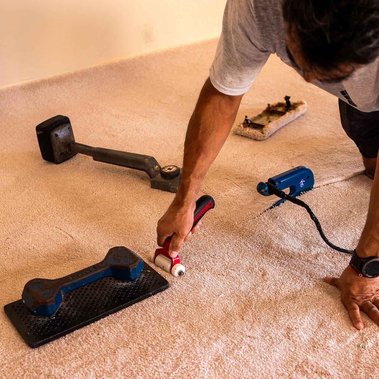 A man skillfully cutting carpet flooring with a tool, ensuring an accurate fit for installation.
