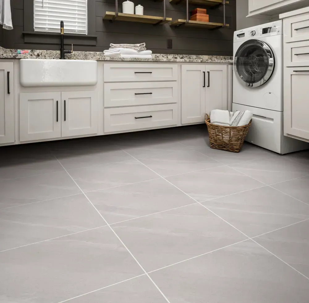 a large laundry room with dark walls, white cabinets, and large gray floor tiles