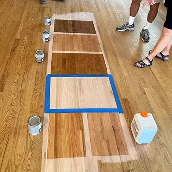 A group of individuals observing a freshly painted hardwood floor in a workshop setting in Aurora, CO.
