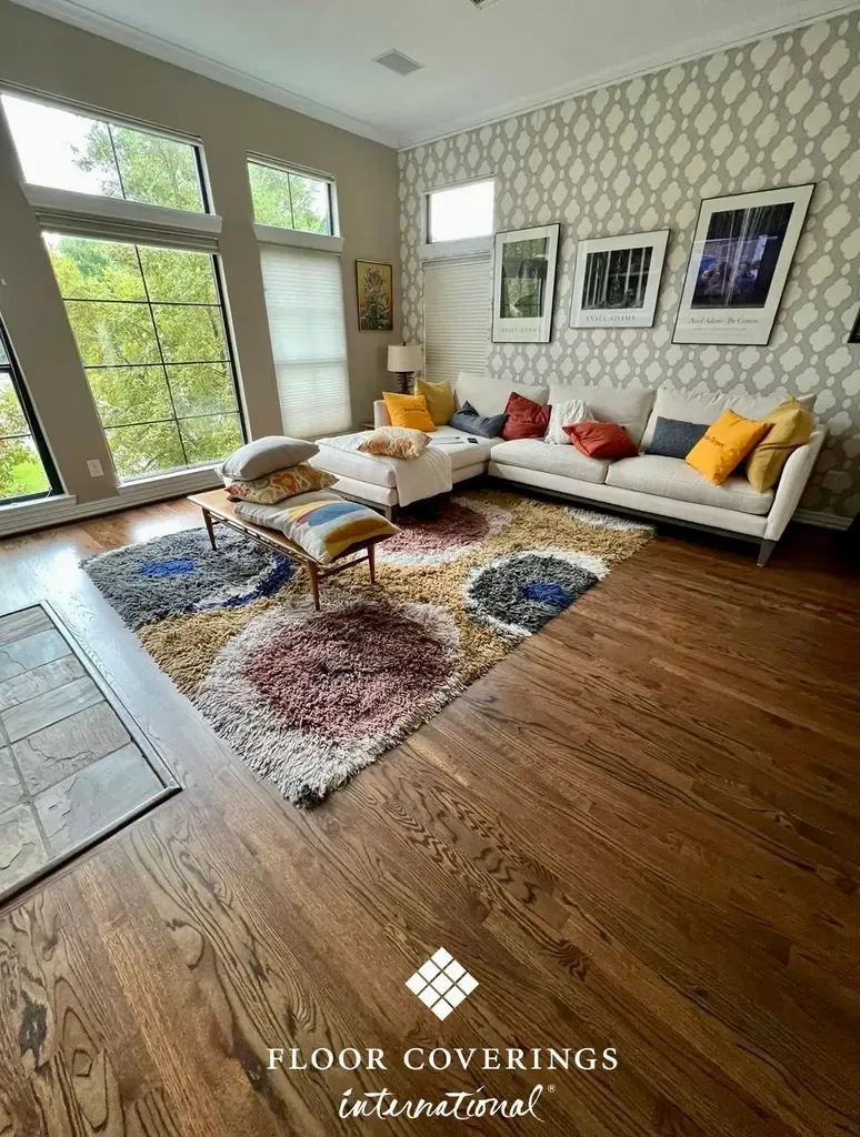 A spacious living room with a couch and large rug, illustrating the quality of hardwood flooring repairs in Houston.