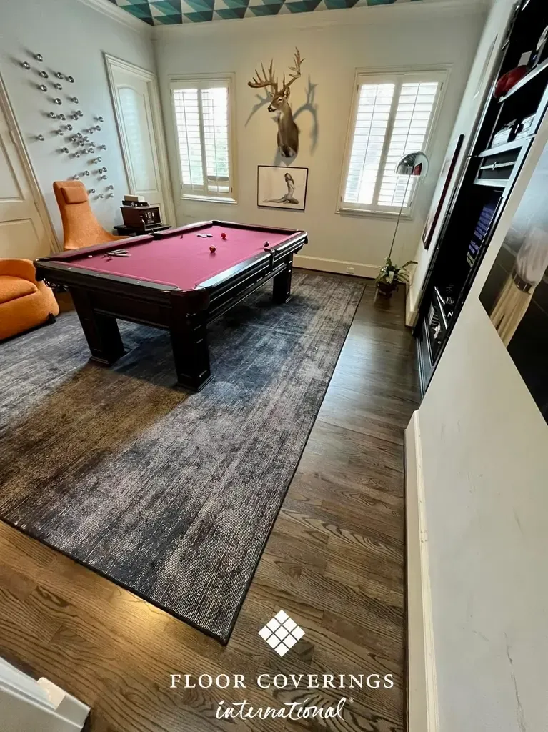 A pool table surrounded by a rug and a couch in a room, emphasizing the elegant hardwood flooring beneath.