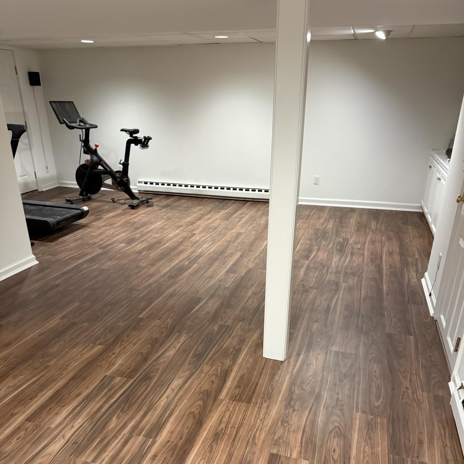 Beautiful luxury vinyl flooring in a dark wood tone on a basement gym floor.