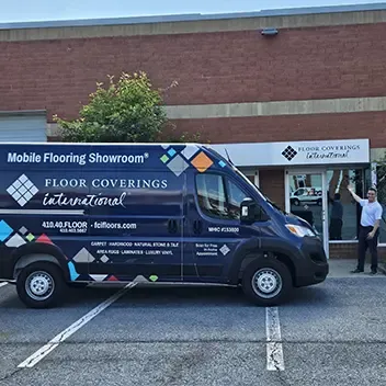 A van is parked outside a building, with a man standing next to it, preparing for flooring work in Owings Mills.