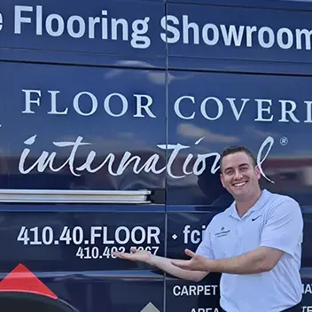 A man poses next to a van marked "Floor Coverings International," indicating services for flooring projects in Owings Mills.