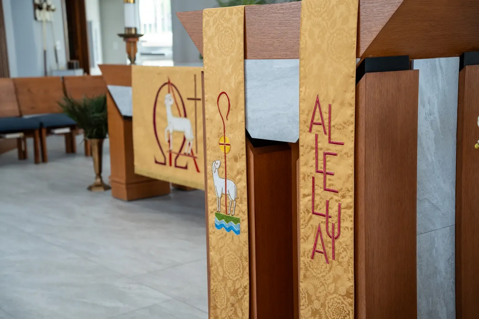Wooden lectern and altar adorned with gold cloth featuring embroidered white lambs and religious symbols, creating a serene church atmosphere.