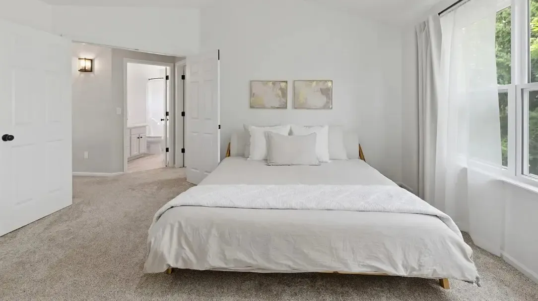 A clean and modern bedroom with a white bed and door, highlighting new flooring in Aurora, CO.