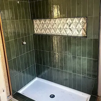 A stylish shower with green tiles arranged in a decorative pattern, highlighting contemporary tile installation in a bathroom.