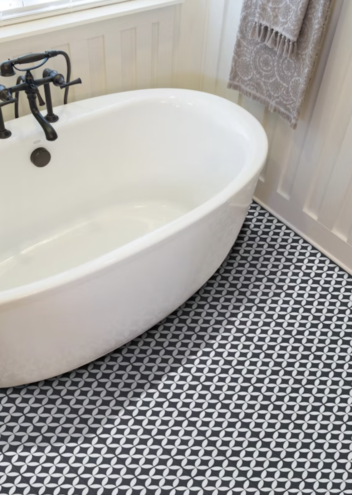 a white soaking tub with black faucet and black and white patterned floor tiles