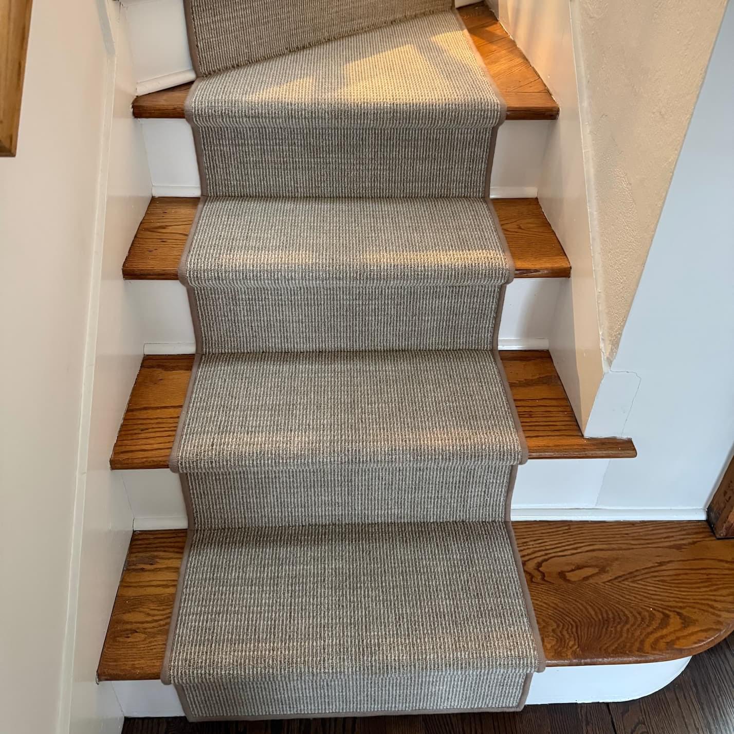 A stairwell with light tone wood treads and a beige runner rug. 